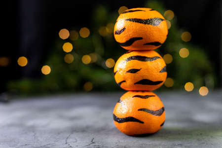 Tangerines with painted stripes on a black background with a Christmas tree. The concept for the new year of the tiger for children. Tiger mandarines for kids fun with golden bokehの写真素材