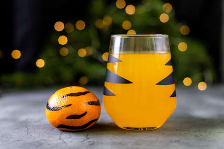 orange mandarin cocktail in glass with black stripes. Christmas holiday welcome drink. Concept for children new year with tree branches and striped tangerines with bokehの写真素材