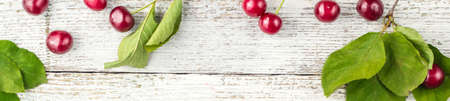 banner of Frame of Red ripe cherry berries and green leaves on white wooden background. Flat lay, top viewの写真素材