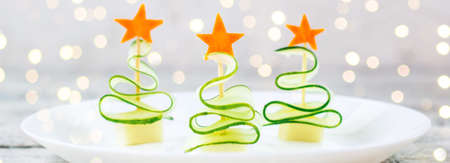 banner of Creative concept set christmas trees of cucumber, cheese and star of carrot. Funny kids food for new year party on white plateの写真素材