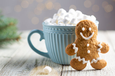 A blue cup of winter hot drink with marshmallows and gingerbread man on a white wooden background. Festive xmas background. Traditional Christmas atmosphere with bokeh. New year holiday concept.の写真素材