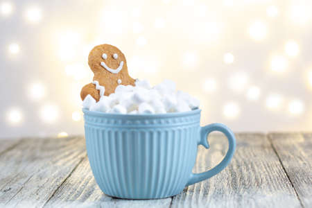 gingerbread man in a blue cup of winter hot drink with marshmallows on a white wooden background. Festive xmas background. Traditional Christmas atmosphere with bokeh. New year holiday concept.の写真素材