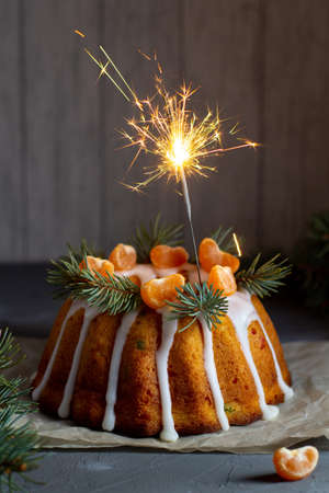 Christmas cake with candied fruits decorated with icing mandarin slices and fir branches with sparklers. Xmas holiday New Year celebration conceptの写真素材