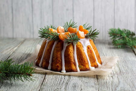 Homemade Christmas cake with candied fruits decorated with icing mandarin slices and fir tree branches. Xmas holiday New Year celebration concept on white wooden tableの写真素材