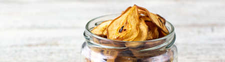 banner of A pile of dried slices of pears in glass jar on white wooden background. Dried fruit chips. Healthy vegan foodの写真素材