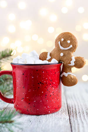 A red cup of winter hot drink with marshmallows and gingerbread man on a white wooden background....