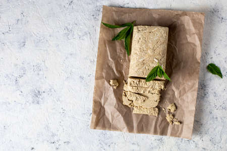 Cutted halva on craft paper. Sweet dessert with mint leaves on white background. Top view with...