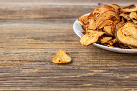 A pile of dried pears in slices on a white plate on wooden background. Dried fruit chips. Healthy food. with copyspaceの写真素材
