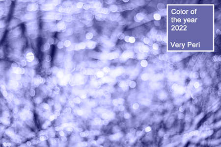winter snow blurred background in city park, snowfall in forest, tree branches covered with snow, abstract snowflakes in blur in very peri trendy color of the year 2022. background.の写真素材