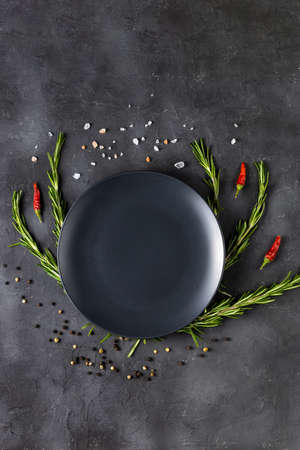Empty black plate with rosemary branches and spices on a dark background. top view with copy spaceの写真素材
