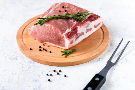 A piece of raw fresh pork with rosemary on a cutting board on a white background. Meat with spices for recipes and cookingの写真素材