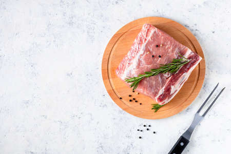 A piece of raw fresh pork with rosemary on a cutting board on a white background. Meat with spices for recipes and cooking. top view with copy spaceの写真素材