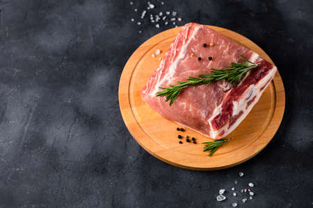 A piece of raw fresh pork with rosemary on a cutting board on dark background. Meat with spices for recipes and cookingの写真素材