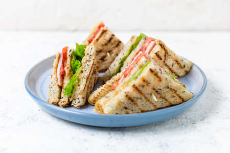 sandwich with ham cheese tomatoes lettuce onions on plate. Classic club sandwich with whole grain bread on white background.の写真素材