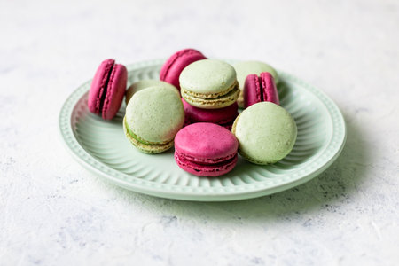 Pink and green macaroons on green plate on light white background. Traditional French sweet dessert.の写真素材