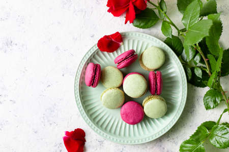 Pink and green macaroons on green plate and red rose on light white background. Traditional French sweet dessert. top view with copy spaceの写真素材