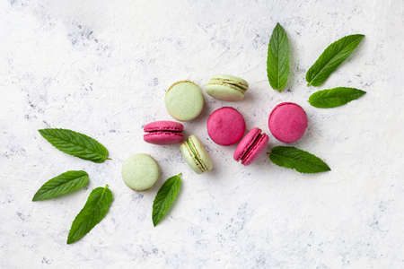 Design of green and pink macarons with mint leaves on light white background. Traditional French sweet dessert. top view, copy spaceの写真素材