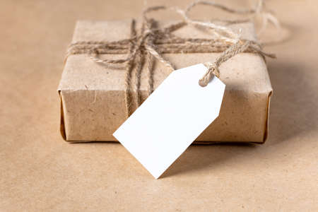 empty white gift tag mock up on craft paper box on natural beige background. Minimal boho style