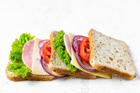 sandwich with ham cheese tomatoes lettuce onions. Ingredients for a sandwich with whole grain bread on a white background. top viewの写真素材