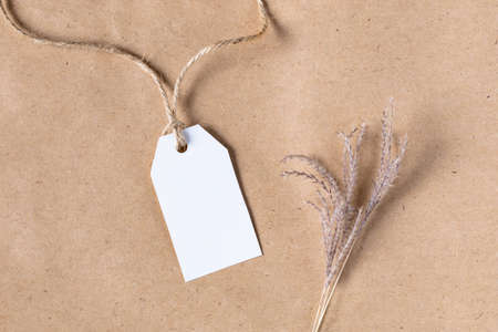 White product tag empty label for mock up with dried spikelets decoration on craft beige background. Flatlay, top view with copyspace, mock up. Minimal boho styleの写真素材