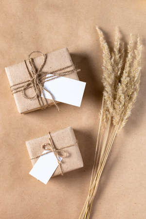empty white gift tag mock up on craft paper box with dried spikelets decoration on beige background. Flatlay, top view with copyspace, mock up. Minimal boho styleの写真素材