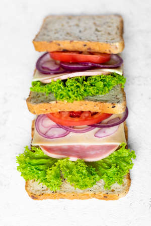 sandwich with ham cheese tomatoes lettuce onions. Ingredients for a sandwich with whole grain bread on a white background. top viewの写真素材