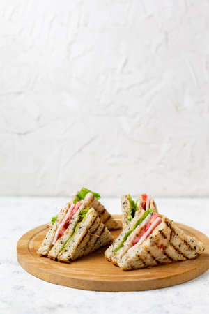 sandwich with ham cheese tomatoes lettuce onions on cutting board. Classic club sandwich with whole grain bread on white background.の写真素材