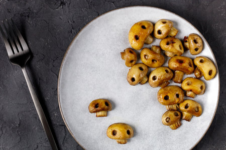 Round plate with mushrooms in the form of skulls and fork on white table. Edible Halloween Concept...
