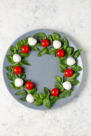Caprese salad in the form of a Christmas wreath. Festive tomato mozzarella and basil appetizer on gray plate. top view with copyspaceの写真素材