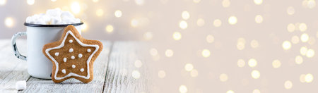 banner of a white cup of winter hot drink with marshmallows and gingerbread star on a white wooden background. Traditional Christmas atmosphere with bokeh. New year holiday concept with copy spaceの写真素材