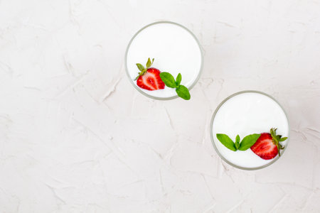 White yogurt with fresh strawberries granola and leaves of mint in two glasses on a white background. healthy breakfast. Copy space, top viewの写真素材