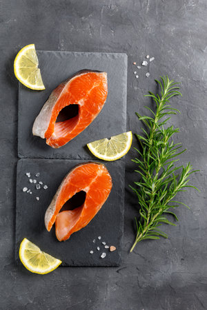 Steak of fresh raw red fish salmon with lemon, rosemary and pepper on black background. top viewの写真素材