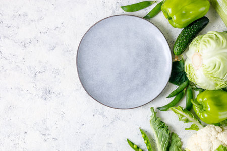 Border of organic green raw vegetables on white table with plate. Top view of healthy organic food background. Copy space, flat layの写真素材
