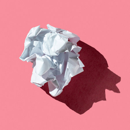 Crumpled white paper sheet in form of ball on a pink background with hard lightの写真素材