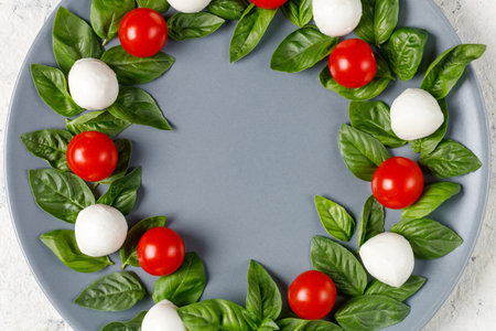Caprese salad in the form of a Christmas wreath. Festive tomato mozzarella and basil appetizer on gray plate. top view with copyspaceの写真素材