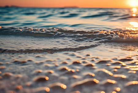Close-up of sea waves touching the shore at sunset, with golden sunlight reflecting on the waterの素材