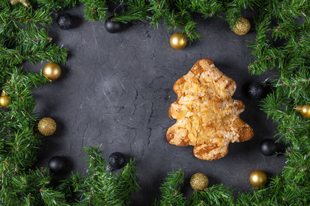 Festive christmas tree pastry with almonds surrounded by pine and baubles on dark stone background.の写真素材