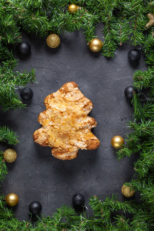 Festive christmas tree pastry with almonds surrounded by pine and baubles on dark stone background.の写真素材
