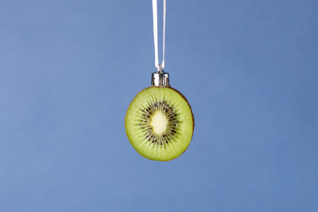 Creative christmas ornament: fresh kiwi slice hanging on white ribbon on blue background.の写真素材