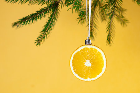 Creative christmas decoration: orange slice ornament hung on pine branch with yellow background.の写真素材