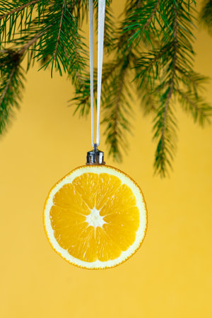 Creative christmas decoration: orange slice ornament hung on pine branch with yellow background.の写真素材