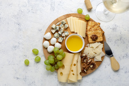 Gourmet cheese platter with grapes, nuts, and honey on rustic wooden board.