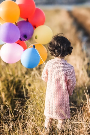 Little girl playing with balloons on wheat fieldの写真素材