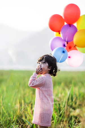 Little girl playing with balloons on wheat fieldの写真素材