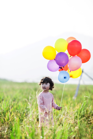 Little girl playing with balloons on wheat fieldの写真素材