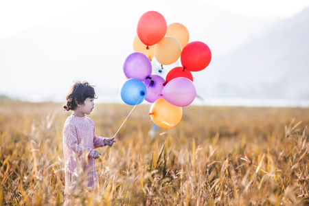 Little girl playing with balloons on wheat fieldの写真素材