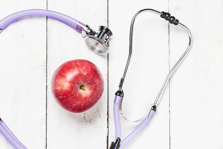 Medical stethoscope and an apple fruit over wooden background. Healthy lifestyle concept image.の写真素材