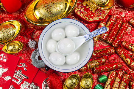 A bowl of tangyuan, red packets and gold ingots on the table. Chinese characters mean luck, wealthの写真素材