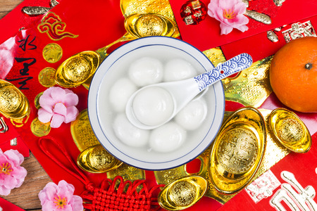 A bowl of tangyuan, red packets and gold ingots on the table. Chinese characters mean luck, wealthの写真素材