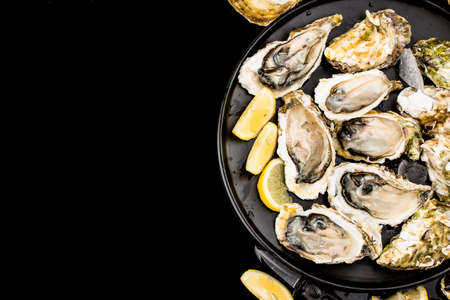 Opened oysters, ice and lemon on a black background.
